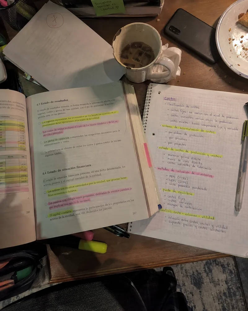 Apuntes de ADE subrayados en tres colores sobre una mesa desordenada